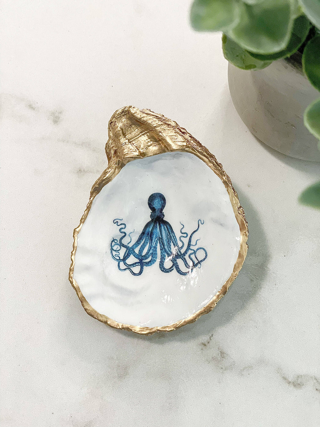 Decorative oyster shell with a blue octopus design on a marble surface.